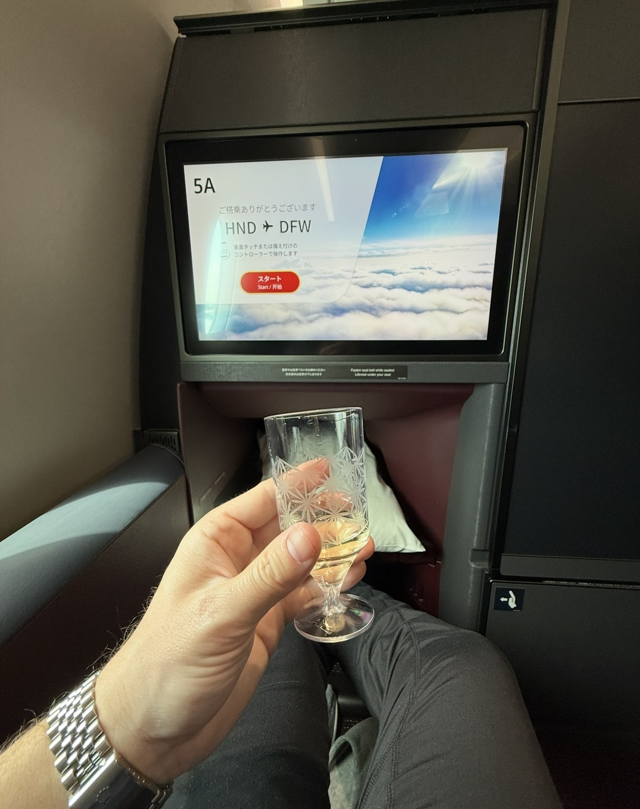 Welcome drink in JAL business class seat 5A, screen showing the HND to DFW routing